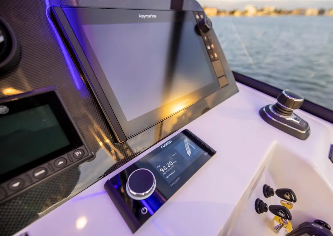 Raymarine multifunction display and Fusion audio control on a boat dashboard, featuring keys and water view in background.